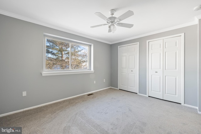 unfurnished bedroom featuring ceiling fan, ornamental molding, light carpet, and two closets