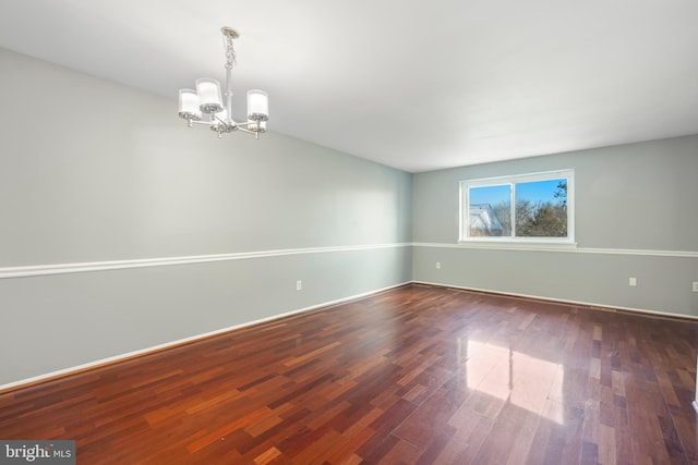 spare room featuring a chandelier and dark wood-type flooring