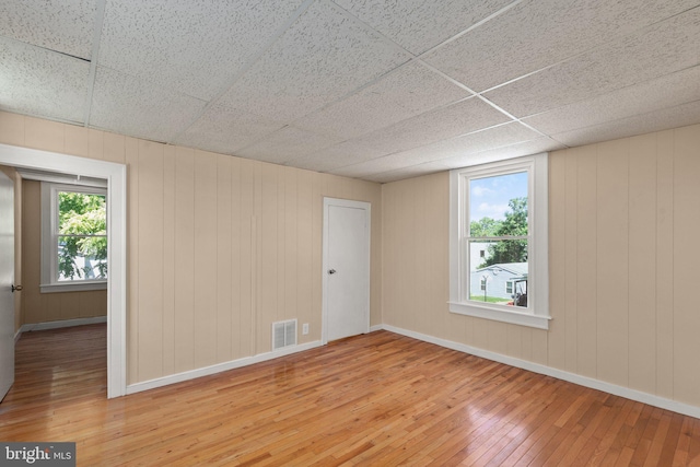 spare room featuring wood-type flooring, plenty of natural light, and a drop ceiling