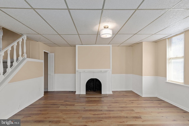 unfurnished living room with wood-type flooring, a healthy amount of sunlight, and a paneled ceiling