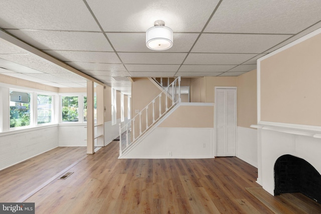 basement with wood-type flooring, a paneled ceiling, and brick wall