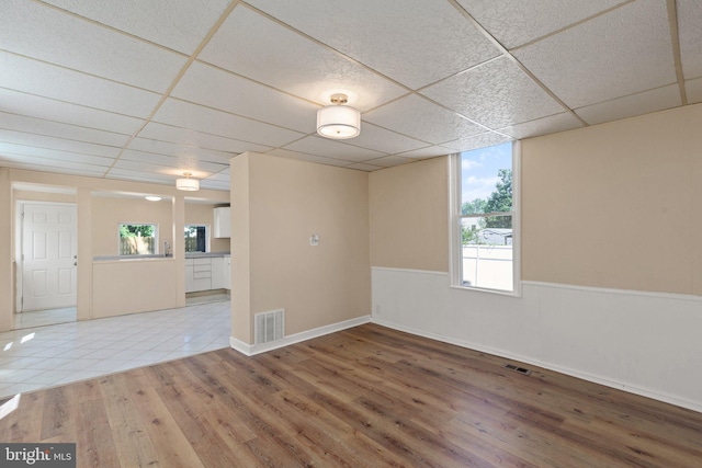 empty room featuring wood-type flooring, plenty of natural light, and a paneled ceiling