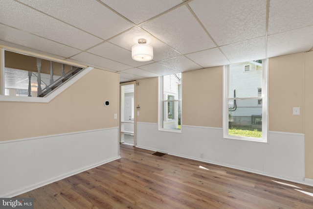 empty room with a wealth of natural light, a paneled ceiling, and hardwood / wood-style floors