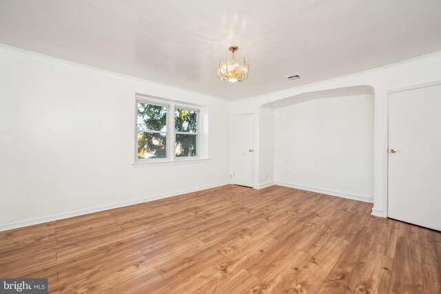 unfurnished room featuring an inviting chandelier, crown molding, and light hardwood / wood-style flooring