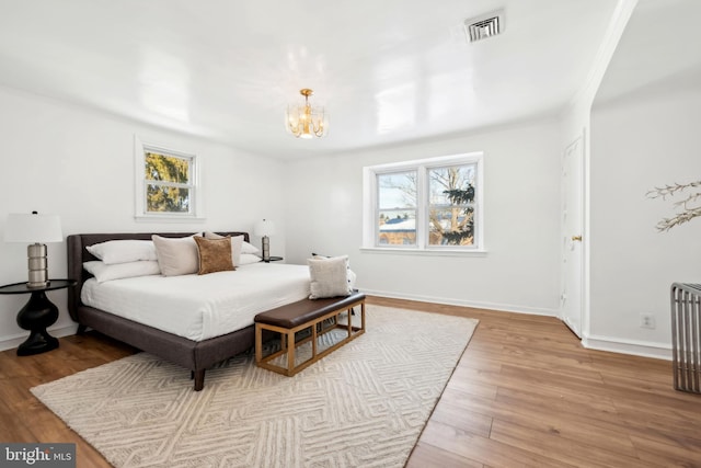 bedroom with multiple windows, radiator heating unit, an inviting chandelier, and light hardwood / wood-style flooring