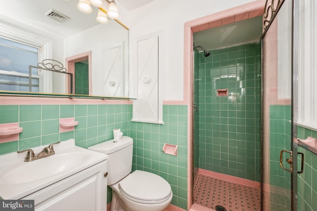 bathroom with tile walls, vanity, a shower with shower door, and toilet