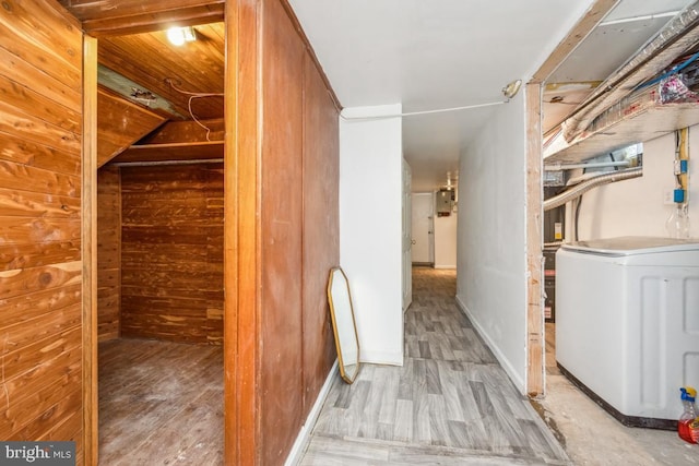 hall featuring washer / clothes dryer, electric panel, light wood-type flooring, and wood walls