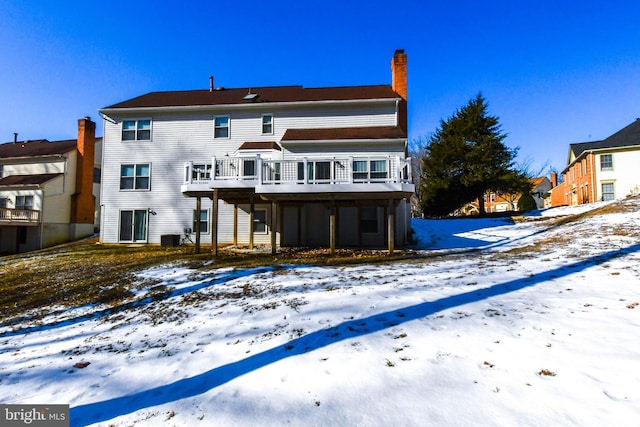 snow covered back of property with a wooden deck and central AC