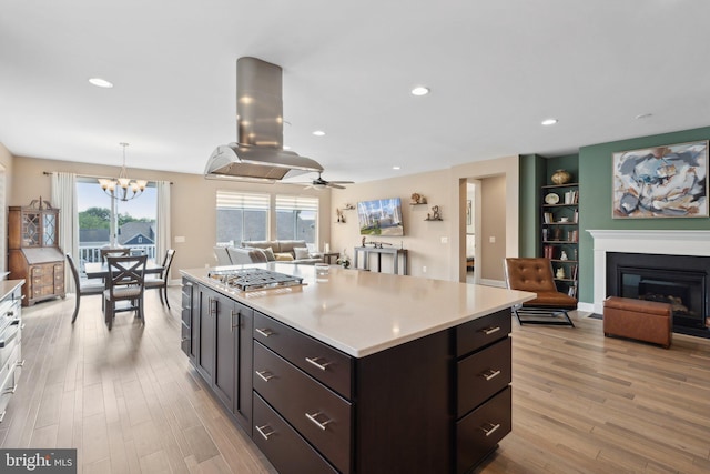 kitchen with light hardwood / wood-style floors, built in shelves, island exhaust hood, decorative light fixtures, and stainless steel gas stovetop