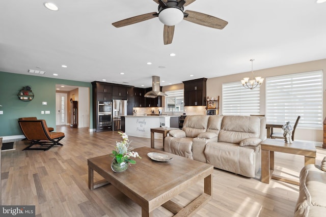 living room with ceiling fan with notable chandelier and light hardwood / wood-style floors