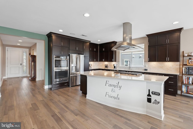 kitchen with backsplash, island exhaust hood, a center island, stainless steel appliances, and light wood-type flooring