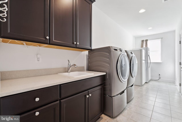 clothes washing area featuring sink, light tile patterned floors, cabinets, and washer and dryer