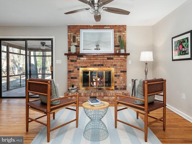 living area featuring a ceiling fan, a fireplace, baseboards, and wood finished floors