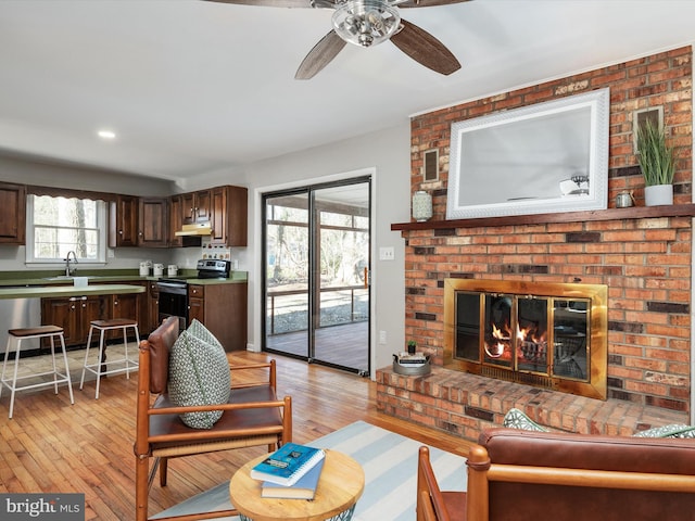 living room featuring light wood-style floors, a fireplace, and ceiling fan