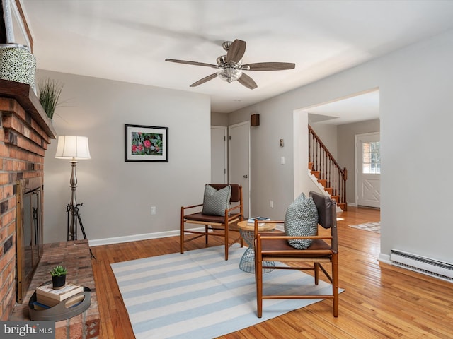 sitting room featuring light wood finished floors, baseboards, a baseboard radiator, stairway, and a fireplace