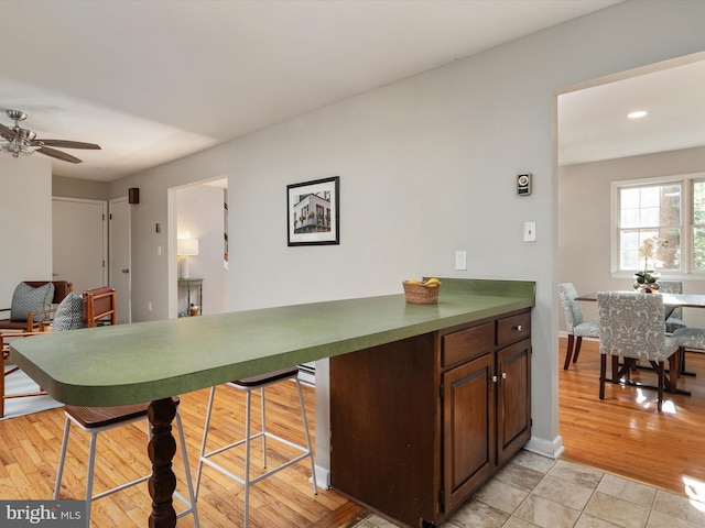 kitchen with light wood finished floors, dark countertops, a ceiling fan, and baseboards