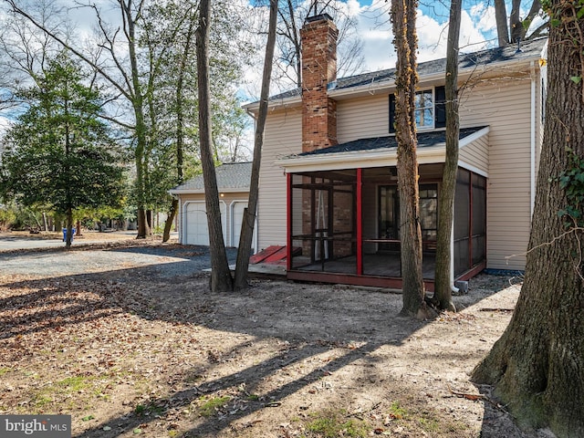 back of property with an outbuilding, a sunroom, a chimney, and an attached garage