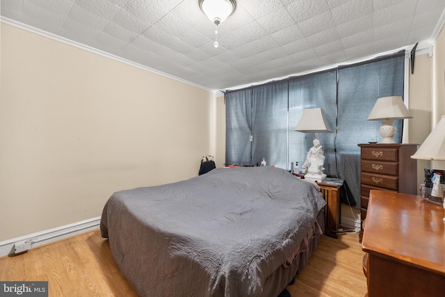 bedroom with crown molding, baseboard heating, and light hardwood / wood-style floors