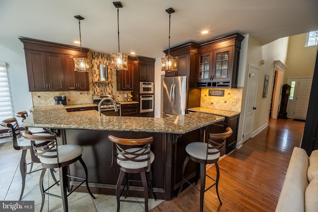 kitchen featuring stainless steel refrigerator, range hood, a breakfast bar area, hanging light fixtures, and dark brown cabinetry