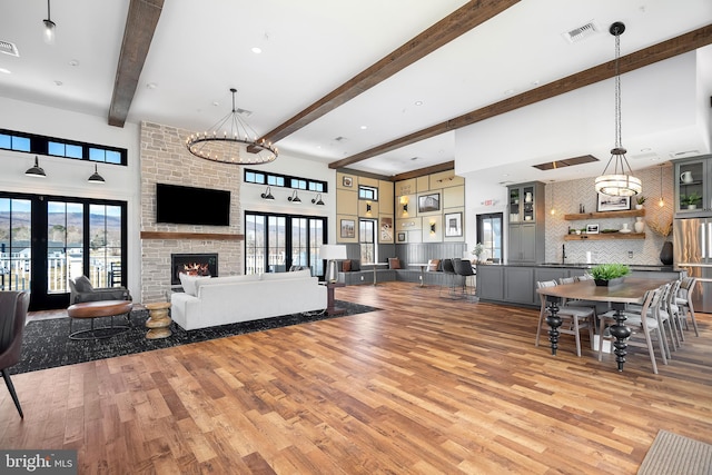 living room with a fireplace, light wood-type flooring, beam ceiling, an inviting chandelier, and a high ceiling