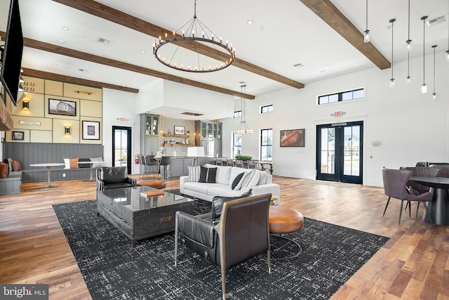 living room featuring french doors, beam ceiling, a high ceiling, hardwood / wood-style floors, and a chandelier