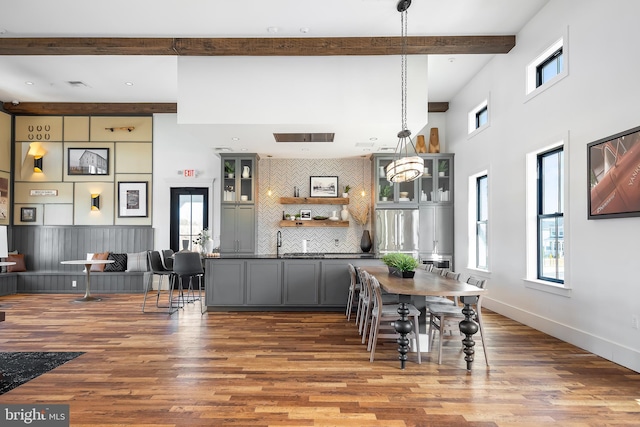 dining area with sink, a towering ceiling, wood-type flooring, and beam ceiling