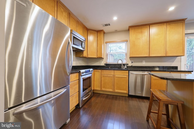 kitchen featuring sink, a breakfast bar area, appliances with stainless steel finishes, dark hardwood / wood-style flooring, and dark stone counters