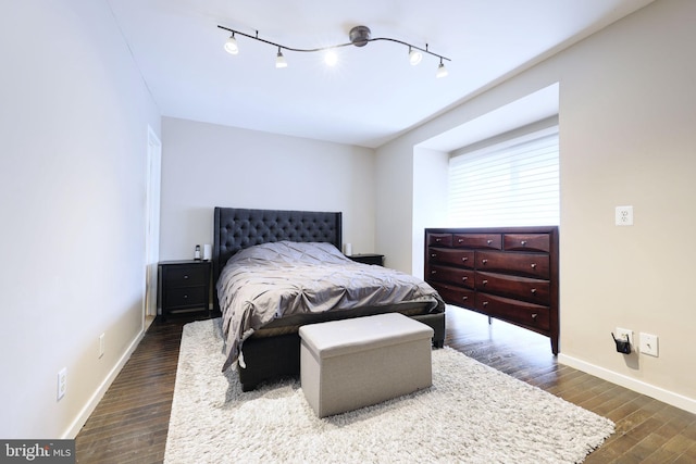 bedroom with rail lighting and dark hardwood / wood-style flooring