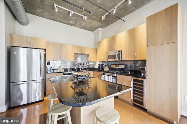 kitchen featuring appliances with stainless steel finishes, a center island, tasteful backsplash, wine cooler, and a breakfast bar