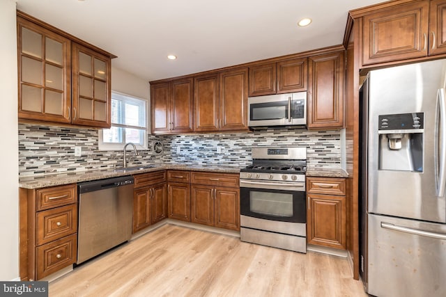 kitchen with tasteful backsplash, light hardwood / wood-style flooring, light stone countertops, and appliances with stainless steel finishes