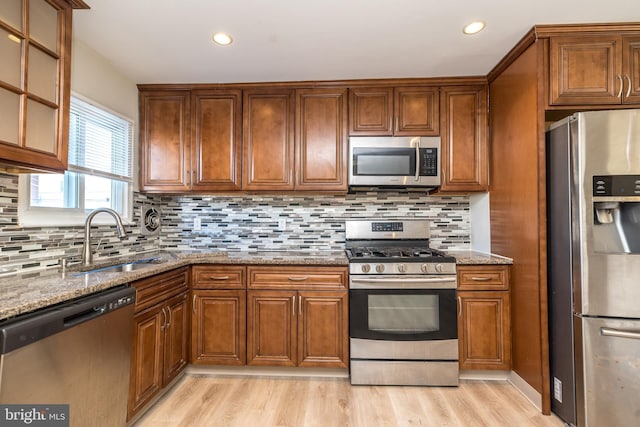 kitchen featuring stone countertops, sink, light hardwood / wood-style floors, and appliances with stainless steel finishes