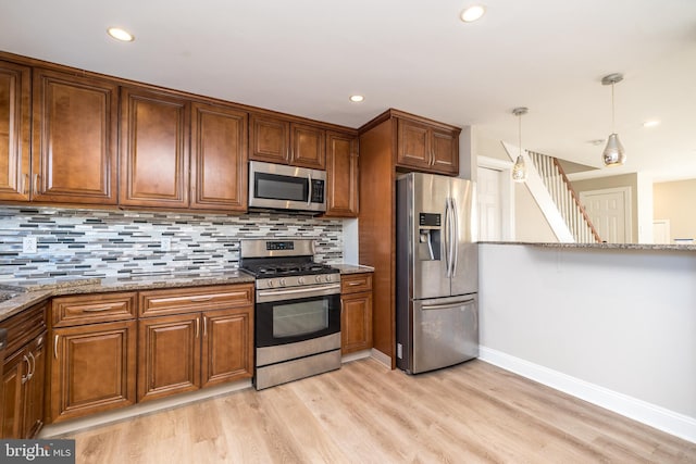 kitchen with tasteful backsplash, hanging light fixtures, appliances with stainless steel finishes, light stone countertops, and light hardwood / wood-style floors