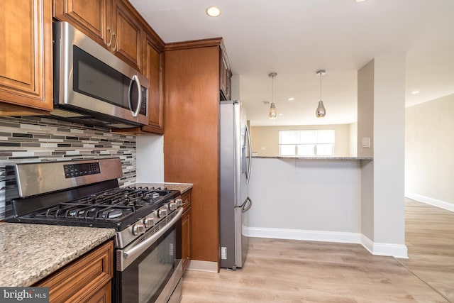 kitchen with light stone counters, hanging light fixtures, light hardwood / wood-style flooring, appliances with stainless steel finishes, and decorative backsplash