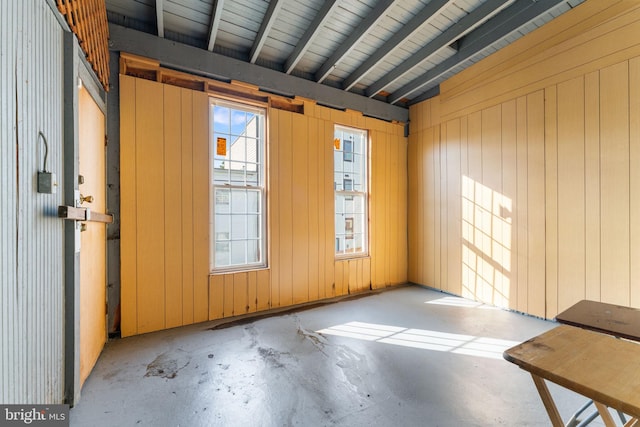 empty room featuring wood walls and vaulted ceiling with beams