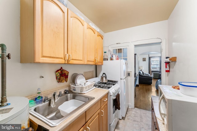 kitchen with light brown cabinetry, sink, white gas range, and radiator heating unit