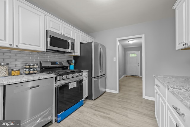 kitchen with stainless steel appliances, white cabinetry, and light stone counters