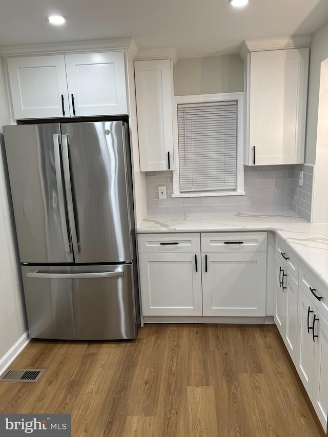 kitchen with light wood-type flooring, white cabinetry, decorative backsplash, and stainless steel fridge