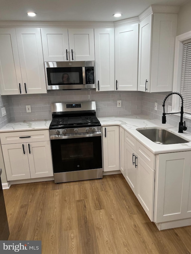 kitchen with sink, white cabinets, tasteful backsplash, and stainless steel appliances