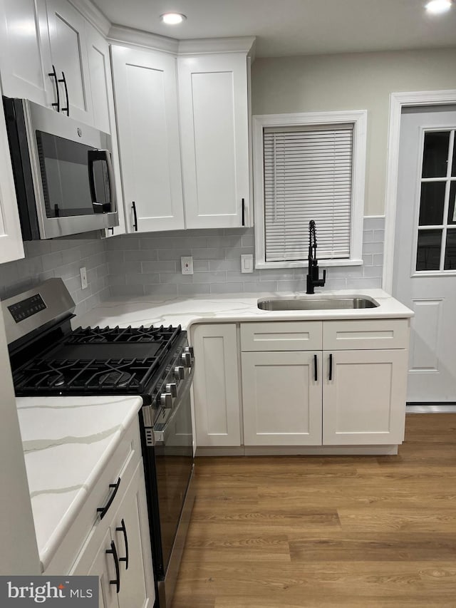 kitchen featuring white cabinetry, sink, light wood-type flooring, backsplash, and stainless steel appliances