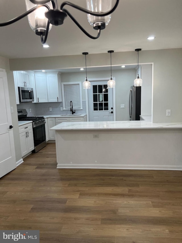 kitchen with appliances with stainless steel finishes, white cabinetry, hanging light fixtures, dark wood-type flooring, and backsplash