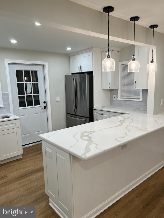 kitchen with light stone countertops, tasteful backsplash, white cabinets, kitchen peninsula, and stainless steel fridge