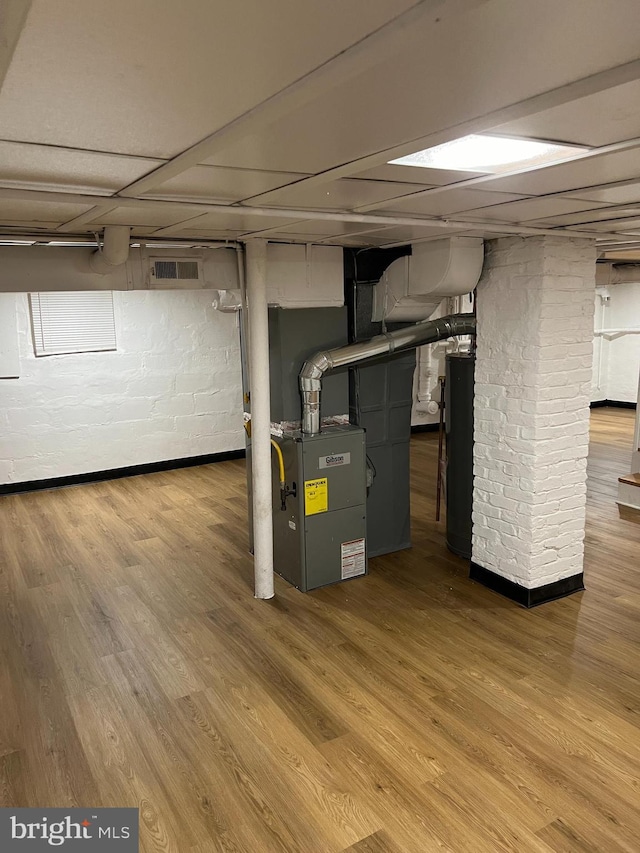 basement featuring hardwood / wood-style floors, heating unit, a paneled ceiling, and water heater