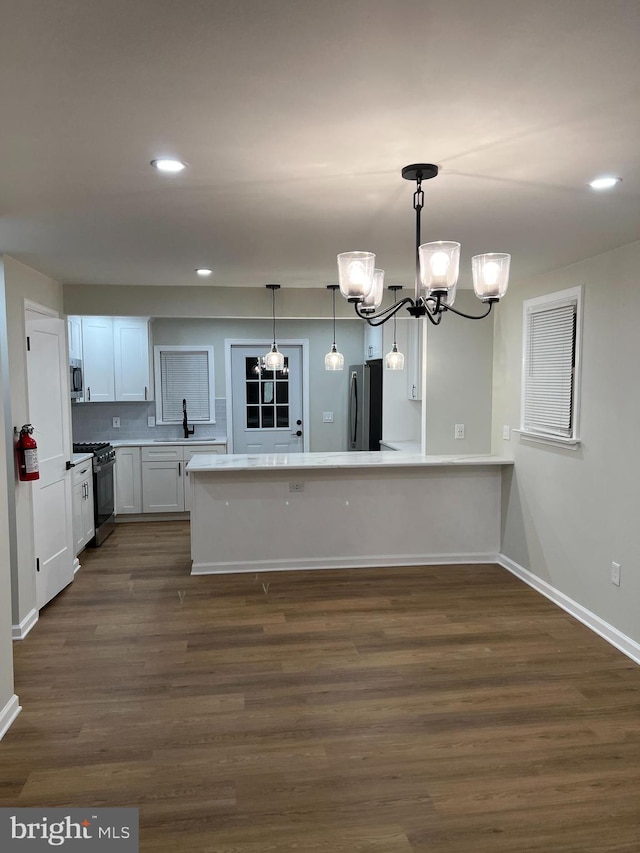 kitchen featuring pendant lighting, backsplash, white cabinets, dark wood-type flooring, and stainless steel appliances