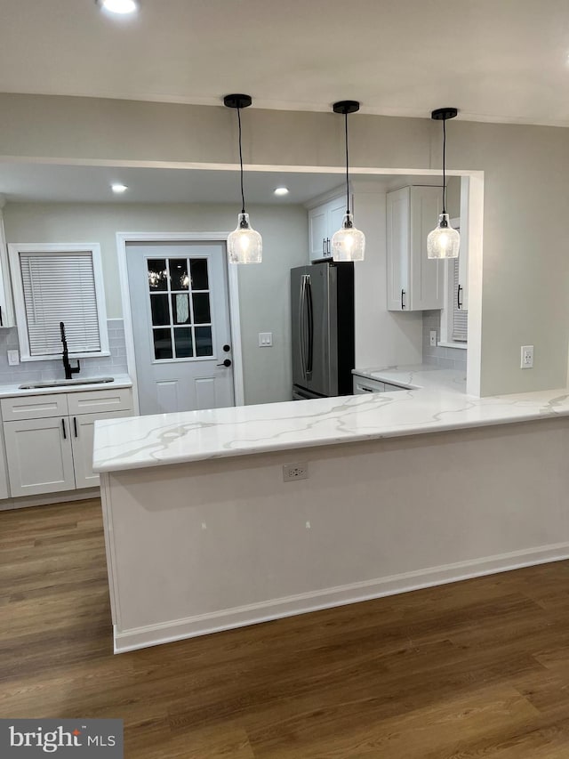 kitchen with tasteful backsplash, stainless steel refrigerator, white cabinets, sink, and kitchen peninsula