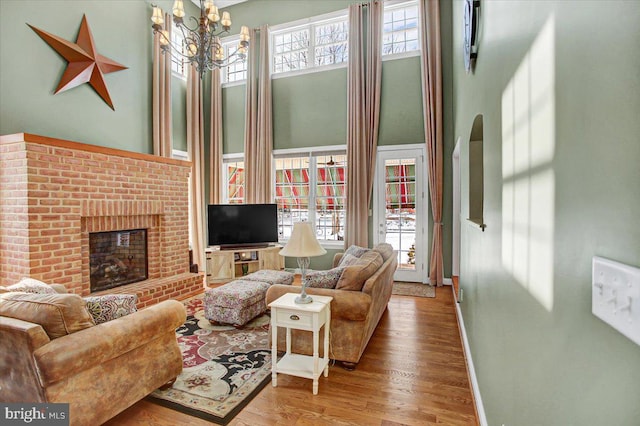 living room with a brick fireplace, a towering ceiling, a notable chandelier, and light wood-type flooring