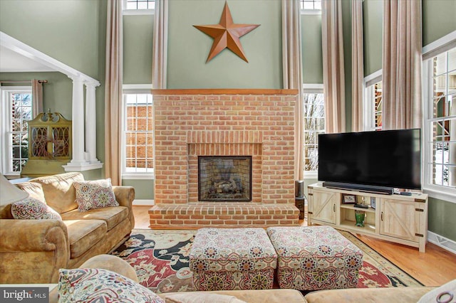 living room featuring wood-type flooring, a fireplace, and ornate columns