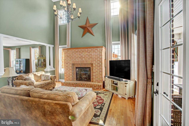 living room with a towering ceiling, a chandelier, a fireplace, and light hardwood / wood-style flooring