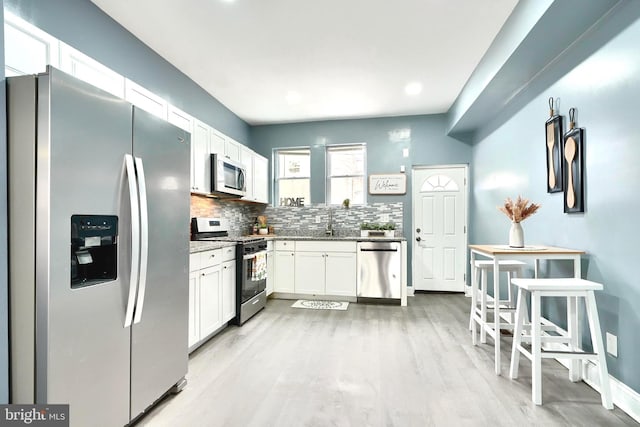 kitchen with sink, backsplash, stainless steel appliances, white cabinets, and light wood-type flooring