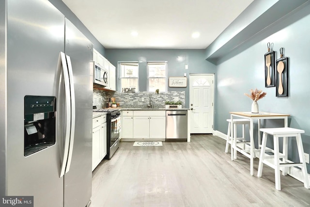 kitchen featuring white cabinetry, sink, decorative backsplash, stainless steel appliances, and light hardwood / wood-style flooring