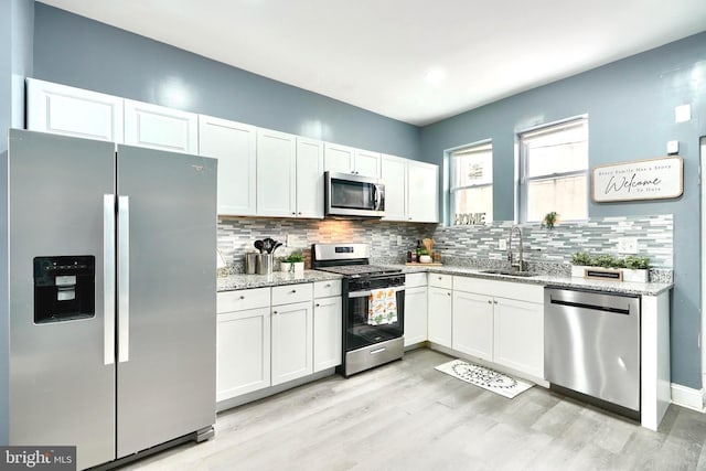 kitchen with light stone counters, stainless steel appliances, sink, and white cabinets